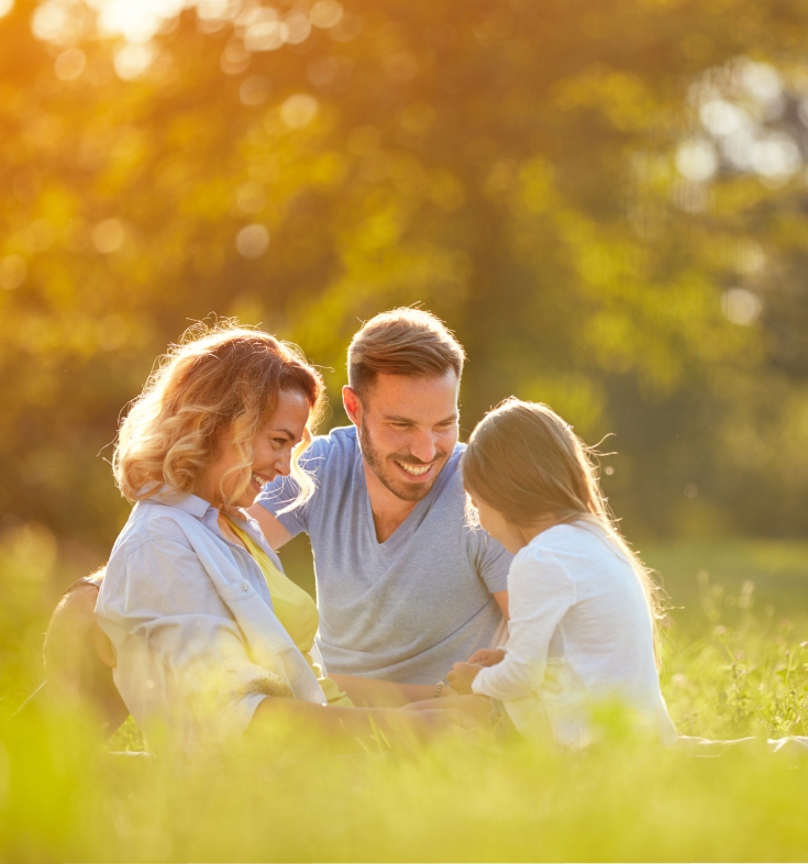 A family happily sitting in a field as they have life insurance.